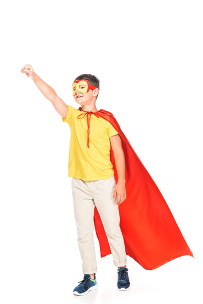 full length view of kid in mask and hero cloak holding fist up isolated on white - Photo, Image