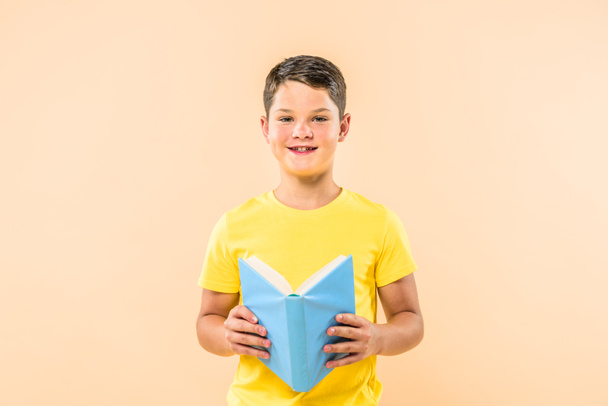 front view of boy in yellow t-shirt holding book isolated on pink - Fotó, kép