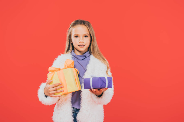 front view of kid holding gift boxes isolated on red - Foto, imagen