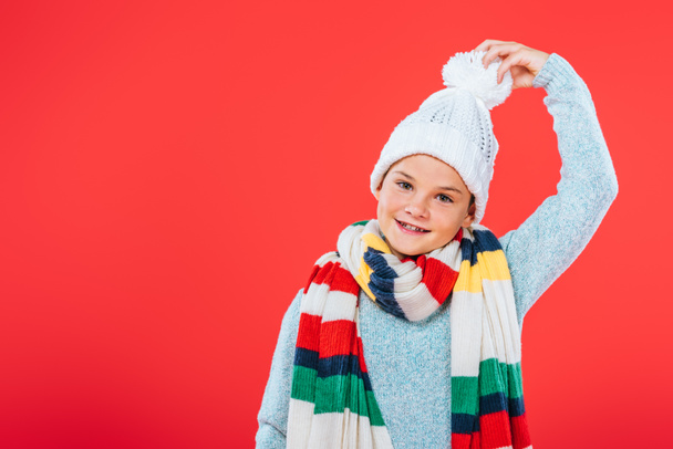 front view of smiling kid in hat and scarf isolated on red - Zdjęcie, obraz