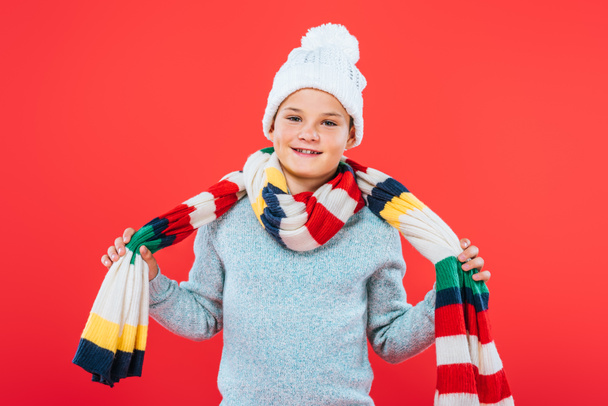front view of smiling kid in hat and scarf isolated on red - Photo, Image