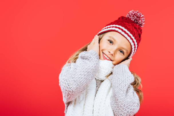 smiling kid in hat and scarf isolated on red - Фото, изображение