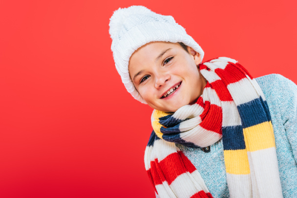 smiling child in hat and scarf isolated on red - Φωτογραφία, εικόνα