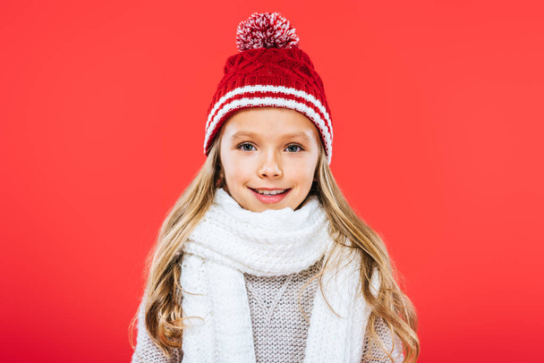front view of smiling kid in hat and scarf isolated on red - Fotó, kép