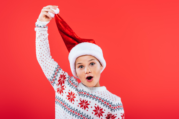 Frontansicht des fröhlichen Kindes in Pullover und Weihnachtsmütze isoliert auf Rot - Foto, Bild