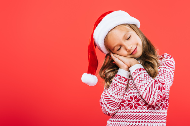 kid in sweater and santa hat sleeping isolated on red - Фото, изображение