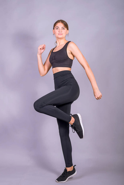 Giovane ragazza magra sta saltando su uno sfondo grigio. Foto di una donna attiva in abbigliamento sportivo
. - Foto, immagini