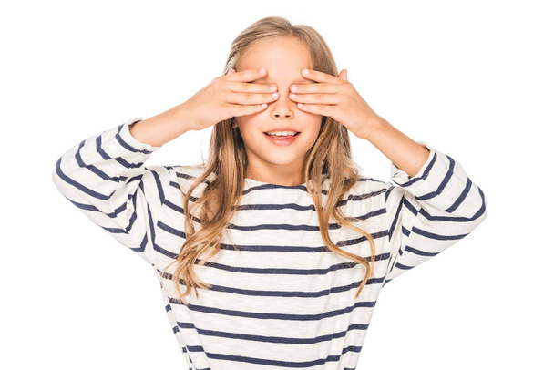 Vorderansicht eines lächelnden Kindes, das die Augen mit isolierten Händen auf Weiß bedeckt - Foto, Bild
