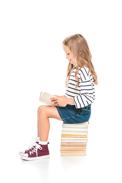 kid in denim skirt sitting on books and reading on white - Zdjęcie, obraz