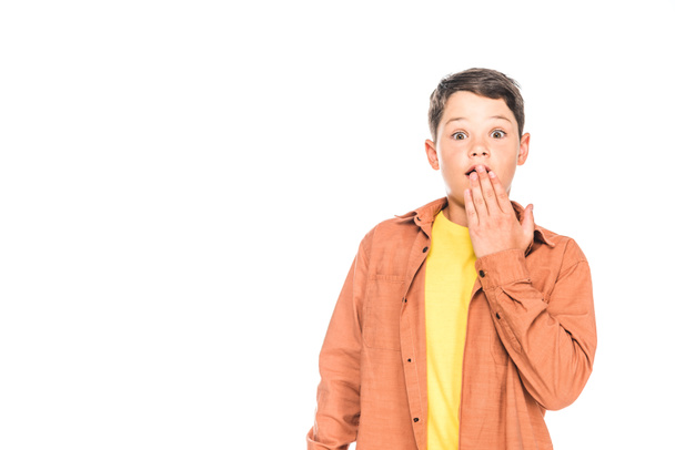 Frontansicht eines schockierten Kindes in lässigem Outfit, das den Mund mit einer isolierten Hand auf Weiß bedeckt - Foto, Bild
