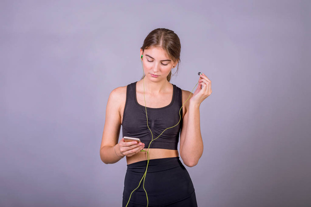 Retrato de mujer joven escuchando música usando auriculares y smartphone en estudio sobre fondo gris
. - Foto, imagen