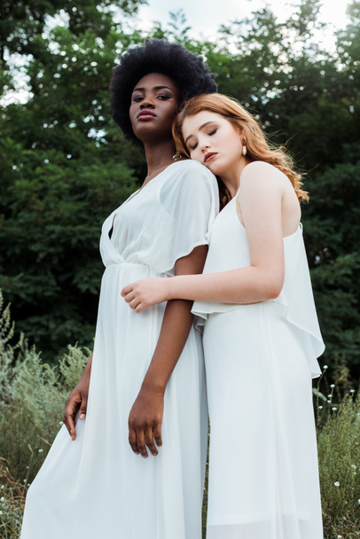 low angle view of pretty redhead girl hugging african american woman outside  - 写真・画像