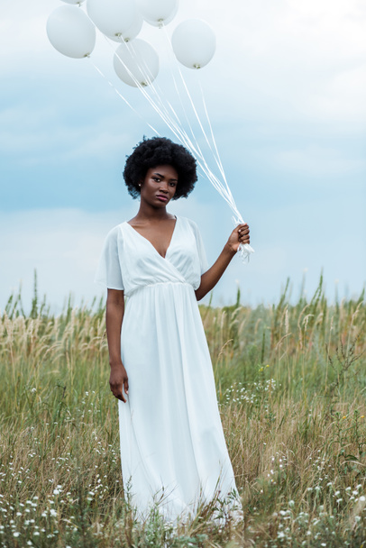 attractive african american girl in dress holding balloons in field  - Photo, image