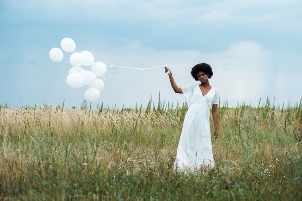 selective focus of african american girl in dress holding balloons in field  - Fotó, kép