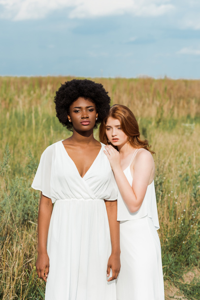 sad redhead woman standing with african american girl in field  - 写真・画像