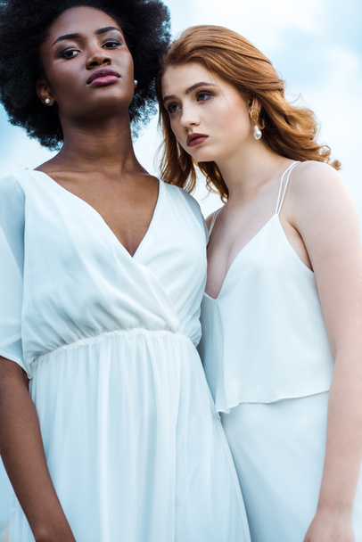 pretty redhead woman standing with african american girl against sky  - Foto, Bild