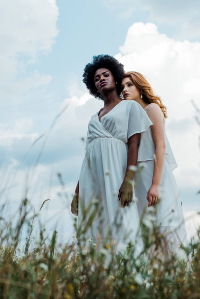 selective focus of redhead girl standing with african american woman against sky  - 写真・画像