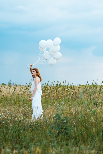 selective focus of redhead girl holding balloons in field  - Фото, зображення