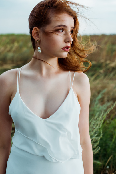 young and beautiful redhead woman in white dress in field  - Фото, зображення