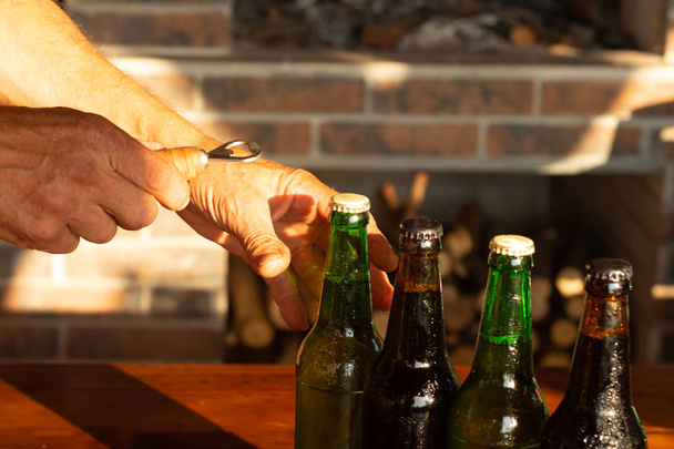 ręka człowiek otwiera brązowy i zielony lód zimne butelki piwa z kropli wody ze starym otwieraczem, zbliżenie - Zdjęcie, obraz