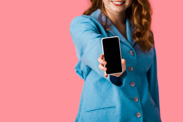 vista recortada de chica pelirroja feliz sosteniendo teléfono inteligente con pantalla en blanco aislado en rosa
  - Foto, imagen