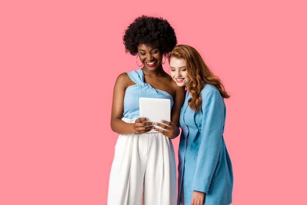 cheerful multicultural girls looking at digital tablet isolated on pink  - Foto, Imagem