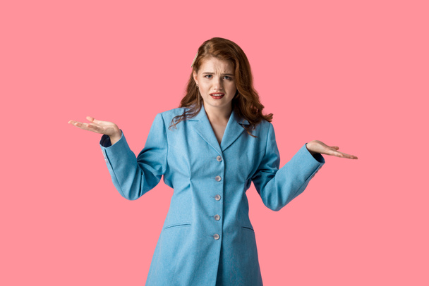 displeased girl looking at camera while showing shrug gesture isolated on pink  - Foto, Imagem