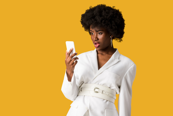 shocked curly african american woman looking at smartphone isolated on orange  - Фото, изображение