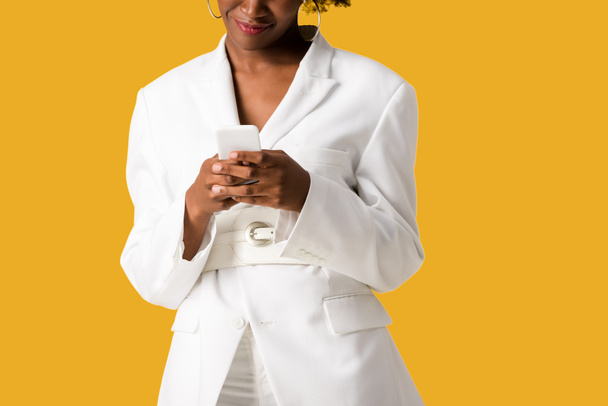 bijgesneden weergave van gelukkig Afro-Amerikaanse vrouw met behulp van smartphone geïsoleerd op oranje  - Foto, afbeelding