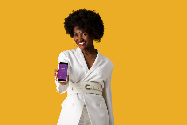 Kijów, Ukraina-9 sierpnia 2019: Happy African American Girl trzymając smartphone z aplikacji Instagram na ekranie izolowane na pomarańczowo  - Zdjęcie, obraz