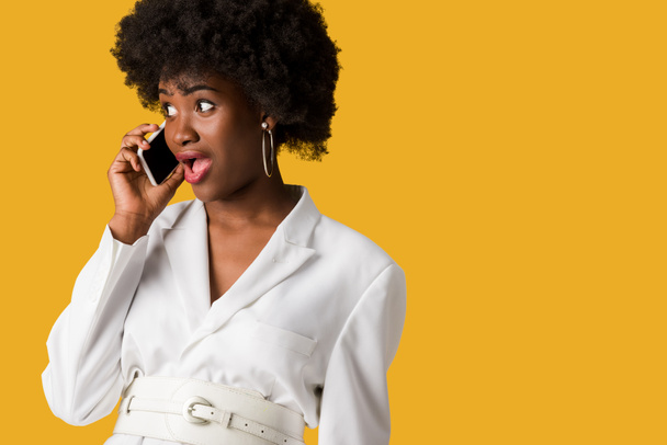 shocked curly african american girl talking on smartphone isolated on orange  - 写真・画像