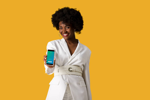 KYIV, UCRANIA - 9 de agosto de 2019: niña afroamericana feliz sosteniendo teléfono inteligente con aplicación de twitter en la pantalla aislada en naranja
  - Foto, Imagen