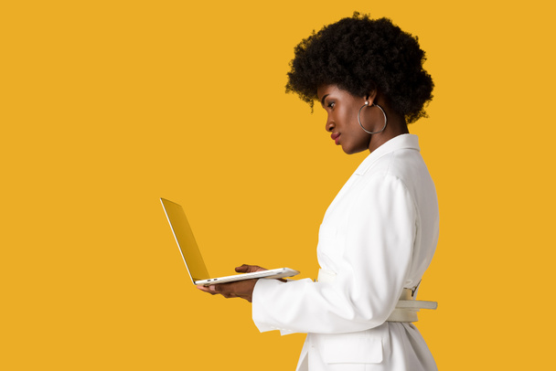 side view of african american girl using laptop isolated on orange  - Φωτογραφία, εικόνα