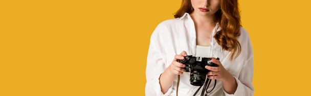 panoramiczny strzał z rudowłosy dziewczyna trzyma cyfrowy aparat fotograficzny izolowany na pomarańczowy  - Zdjęcie, obraz