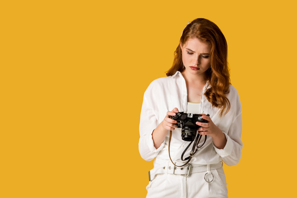 beautiful redhead girl holding digital camera isolated on orange  - Fotó, kép