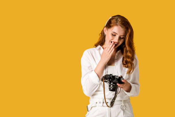 ευτυχισμένος κοκκινομάλλα κορίτσι κρατώντας ψηφιακή φωτογραφική μηχανή απομονωμένη στο πορτοκαλί  - Φωτογραφία, εικόνα