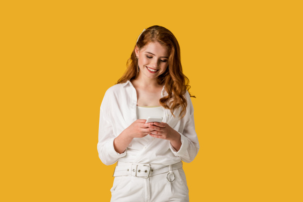 happy redhead girl using smartphone and smiling isolated on orange  - Foto, imagen