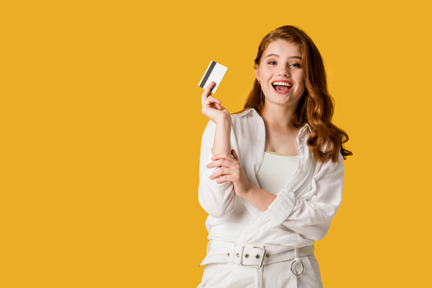 opgewonden jonge vrouw Holding creditcard geïsoleerd op oranje  - Foto, afbeelding