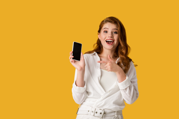 heureux rousse fille pointant du doigt à smartphone avec écran vide isolé sur orange
  - Photo, image