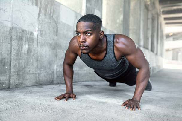 Black male working out alone outside on concrete, pushups in urban downtown city exercise - Photo, Image