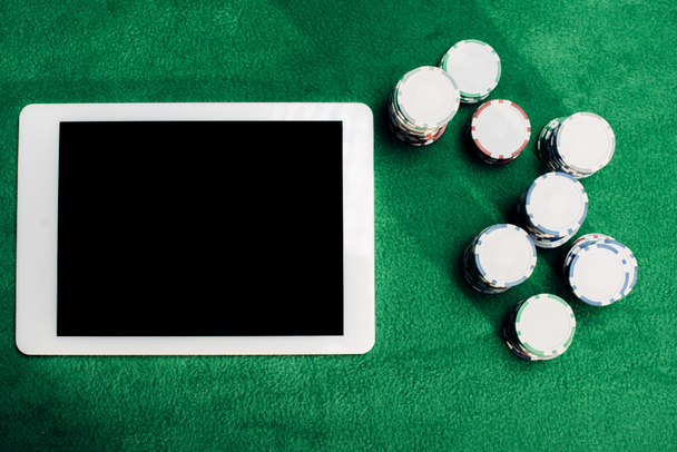 ポーカーテーブル上のポーカーチップの近くに空白の画面を持つデジタルタブレットのトップビュー  - 写真・画像