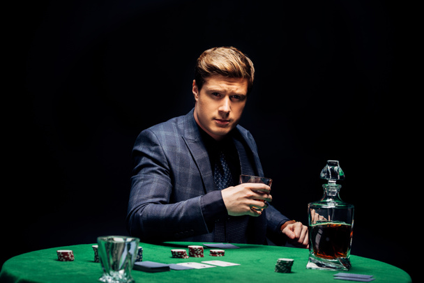 selektivní zaměření pohledného muže, který drží sklo s whisky izolovanou na černém  - Fotografie, Obrázek