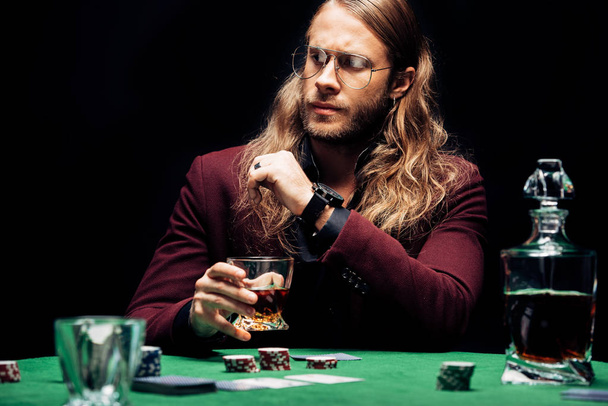 selektivní zaměření vousatého muže v brýlích blízko hrací karty izolované na černém  - Fotografie, Obrázek