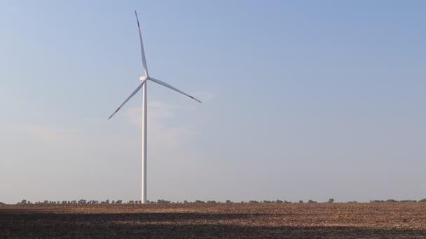 Wind turbine on field. Empty  field in foreground, blue sky  on background. Alternative energy source, production and power generation. Ecology and freedom concept - Footage, Video