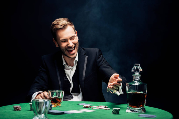 selective focus of happy man holding glass with alcohol on black with smoke  - Photo, Image