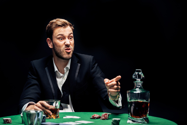 szelektív fókusz dühös férfi ujjal közel alkohol és kártyák elszigetelt fekete  - Fotó, kép