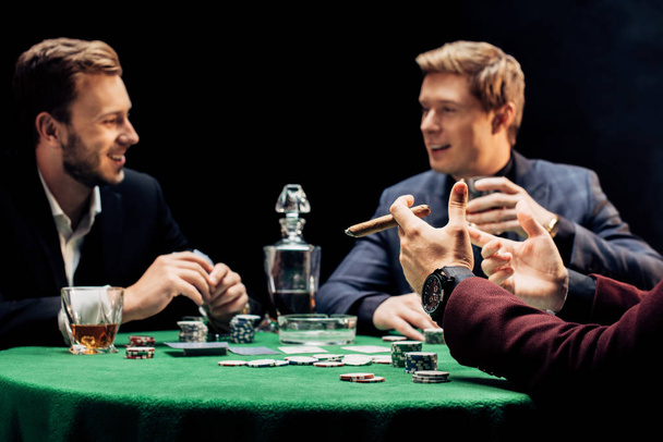 vue recadrée de l'homme tenant cigare près des amis dans le club de poker sur noir
  - Photo, image