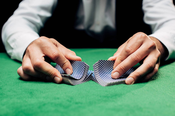 KYIV, UKRAINE - AUGUST 20, 2019: cropped view of croupier holding playing cards near poker table - 写真・画像