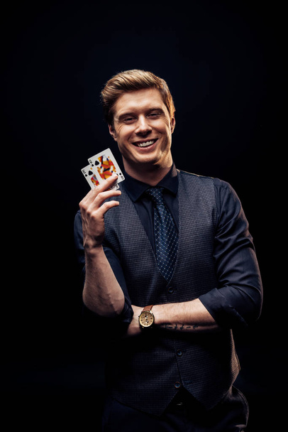 KYIV, UKRAINE - AUGUST 20, 2019: happy man holding playing cards isolated on black  - Foto, Imagen