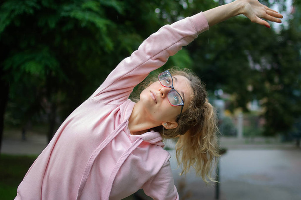 Aktív fitness nő rózsaszín ruhák és szemüvegek is nyúlik a szabadban a parkban tavasszal vagy nyáron reggel. Egészséges életmód koncepció - Fotó, kép